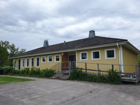 Gul byggnad. Trappa och en ramp leder till öppen ytterdörr.