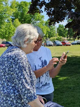 Två kvinnor står i en park och tittar på app i mobilen