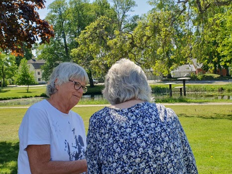 Två kvinnor står i en park och tittar på app i mobilen