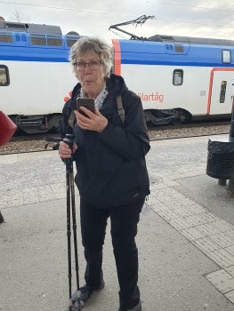 Kvinna på tågperrong. Hon har gåstavar i en hand och mobilen i den andra handen