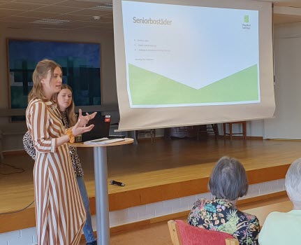 Elin och Lovisa från Vingåkers kommun står vid en talarstol. Vi ser deras presentatio på väggen och en skymt av ett par åhöraren