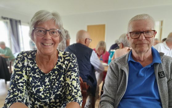En man och en kvinna vid kaffebord. Andra mötesdeltagare syns i bakgrunden