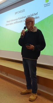 En man med mikrofon står framför en storbild som visas inför en presentation.